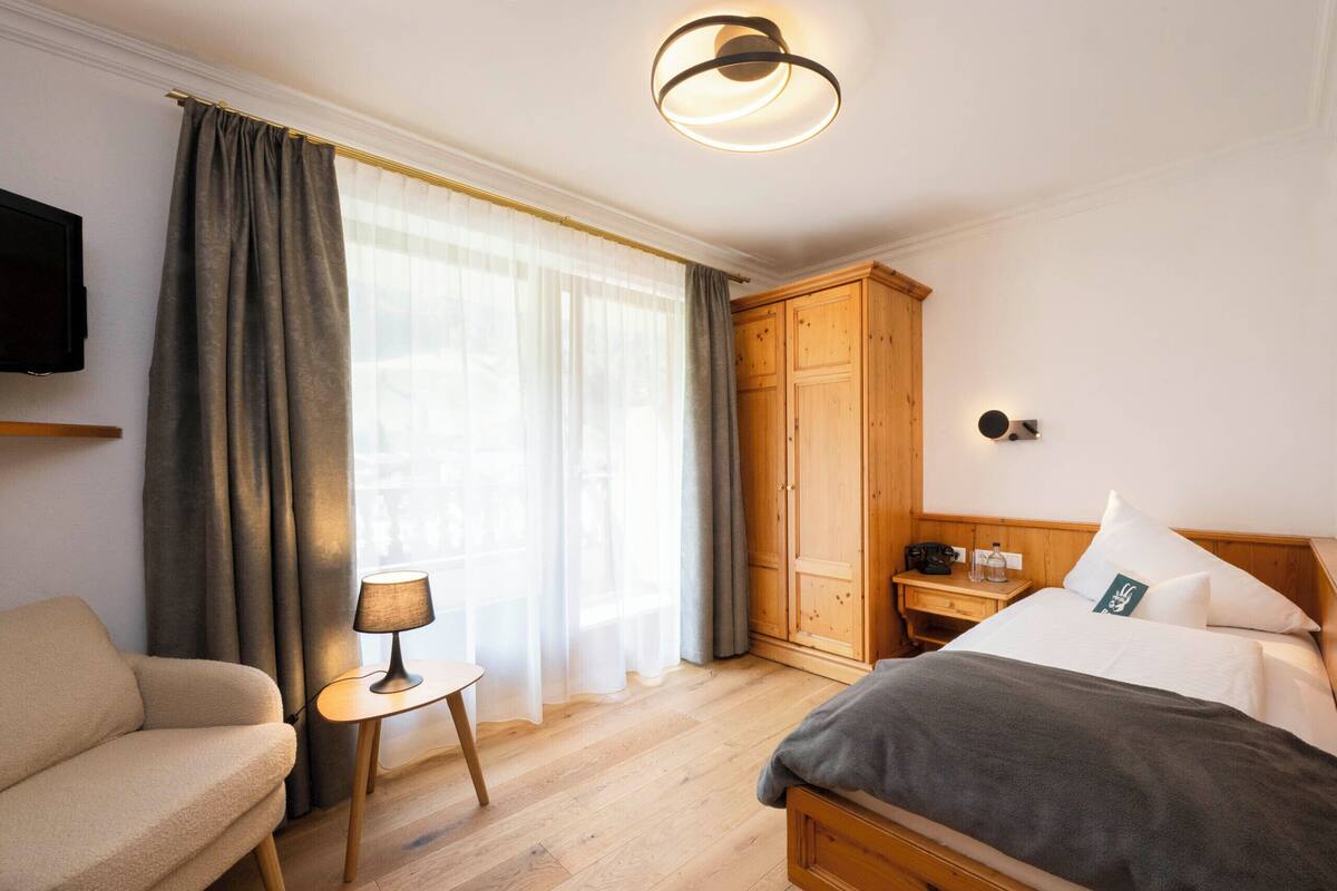 Une chambre d’hôtel comprenant un lit, un canapé, une petite table avec une lampe, une armoire et un téléviseur fixé au mur.