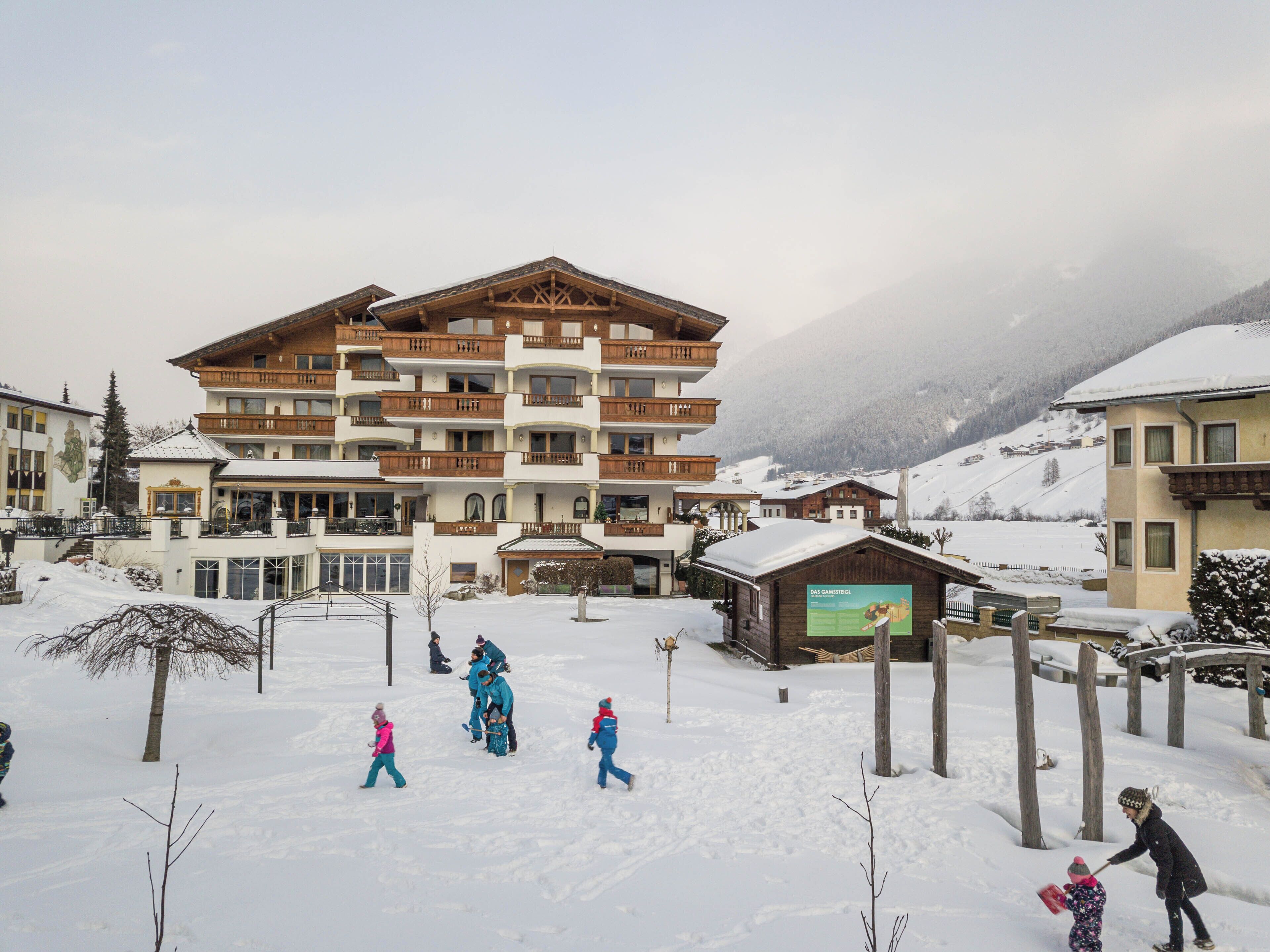 Ein mehrstöckiges Gebäude mit Balkonen, im Hintergrund ein Skigebiet und eine verschneite Landschaft.