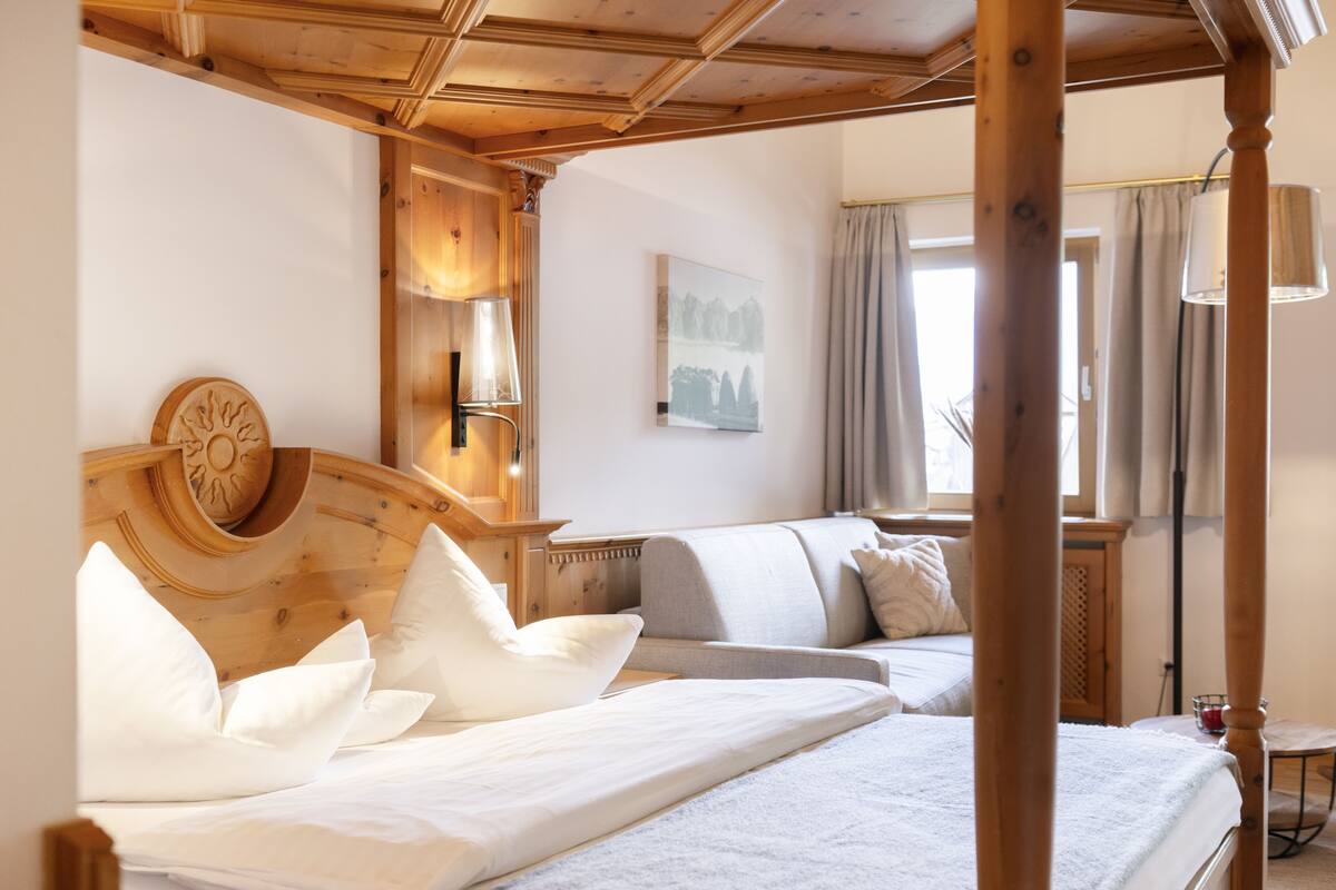 Une chambre à coucher avec une tête de lit en bois, un lit avec une literie blanche, une table de chevet avec une lampe et une fenêtre avec des rideaux.