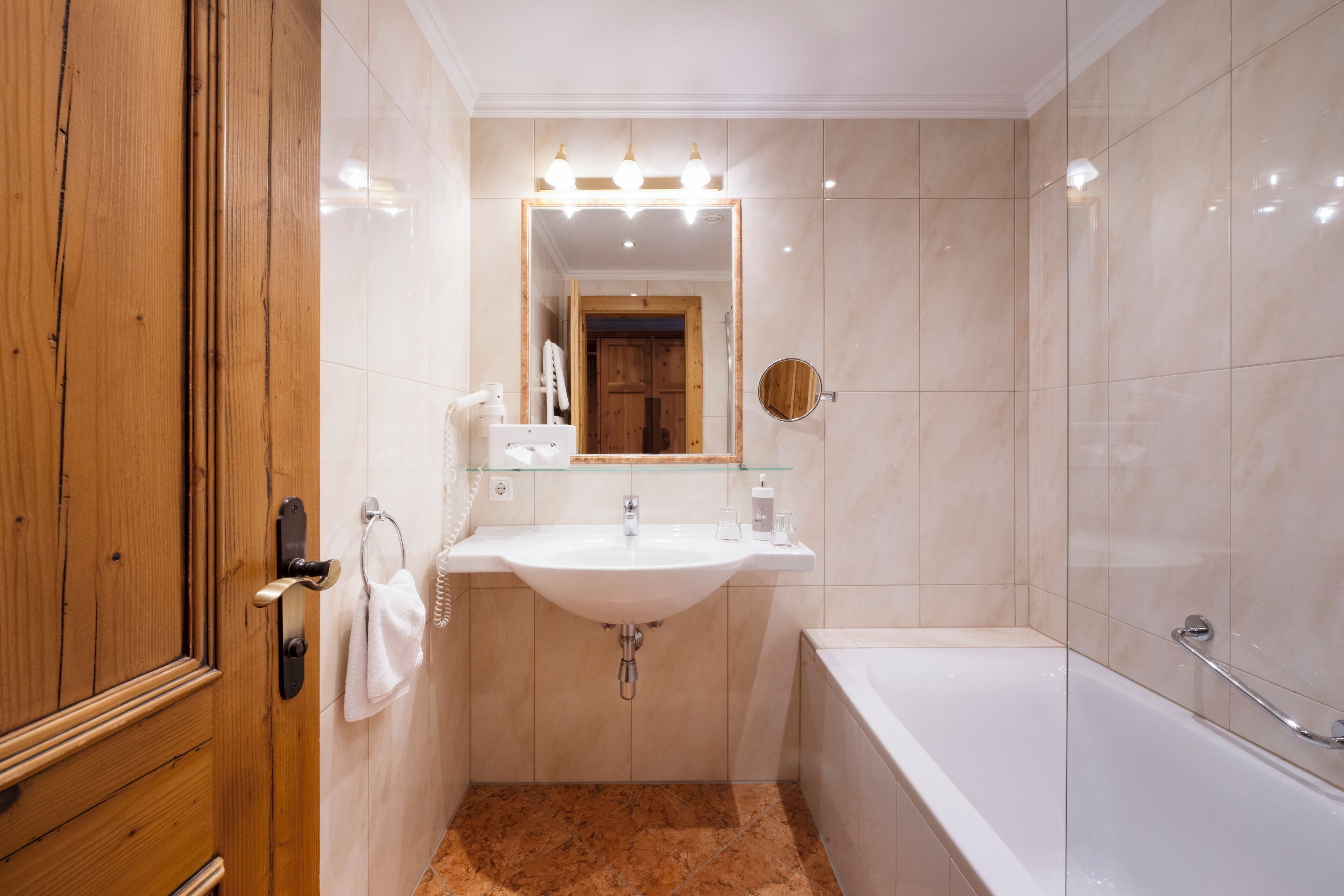 Un bagno con una porta in legno, un lavandino bianco con uno specchio sopra e una vasca da bagno.