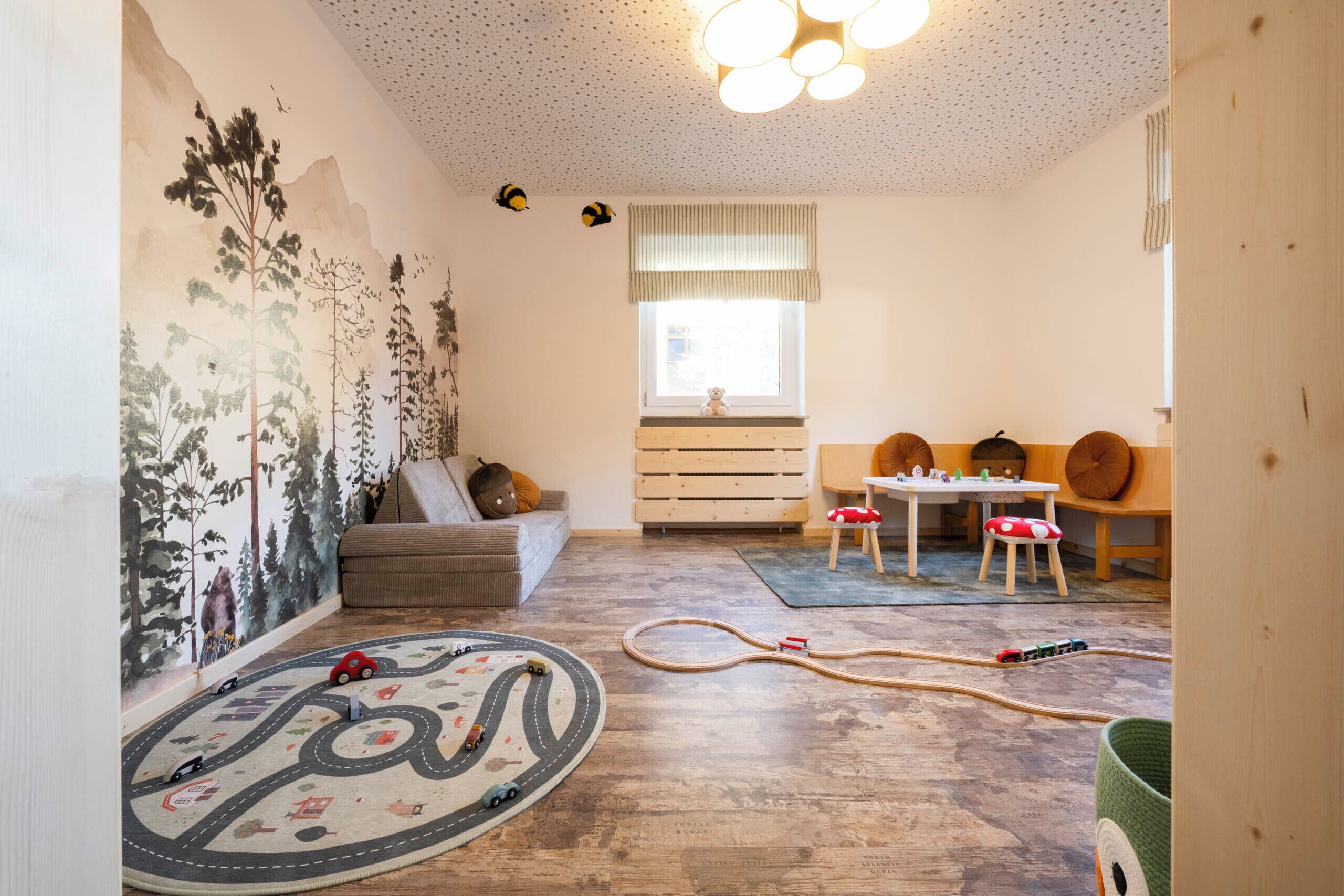 Una sala de estar acogedora con piso de madera, un sofá, una mesa de comedor con sillas y un área de juegos para niños con juguetes y un tapete.