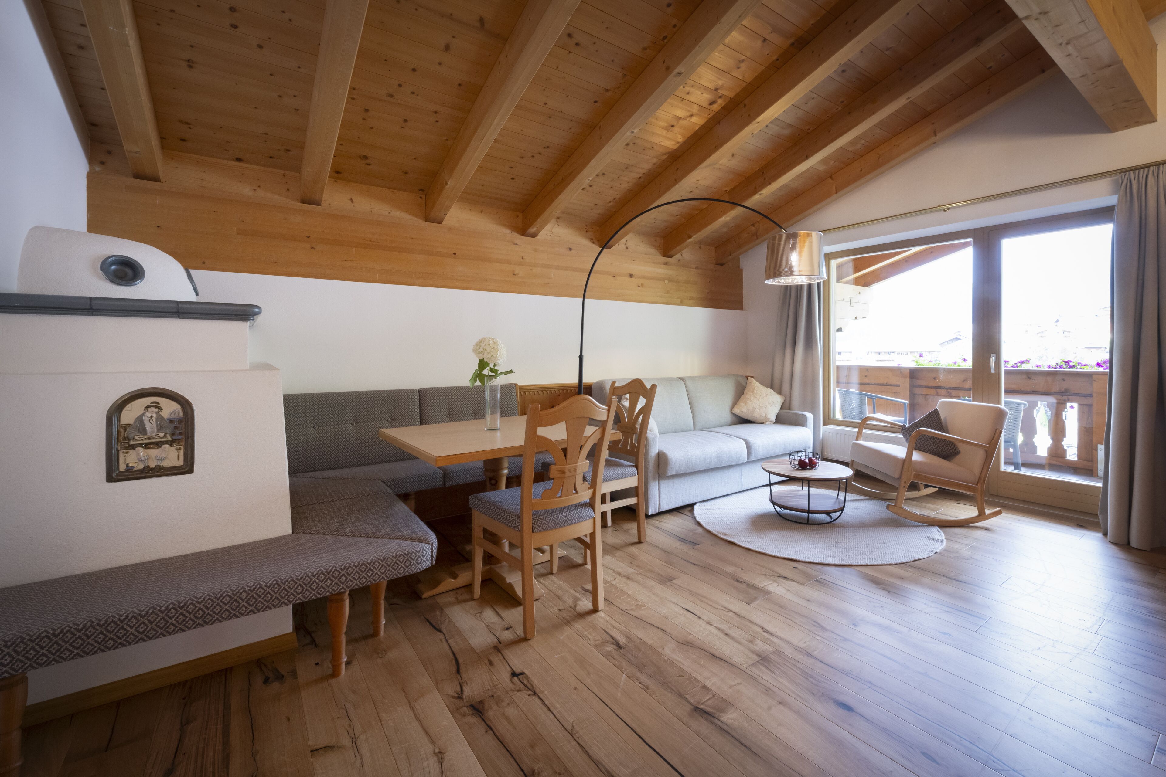 A cozy living room with wooden beams, a sofa, a dining table, and a rocking chair.