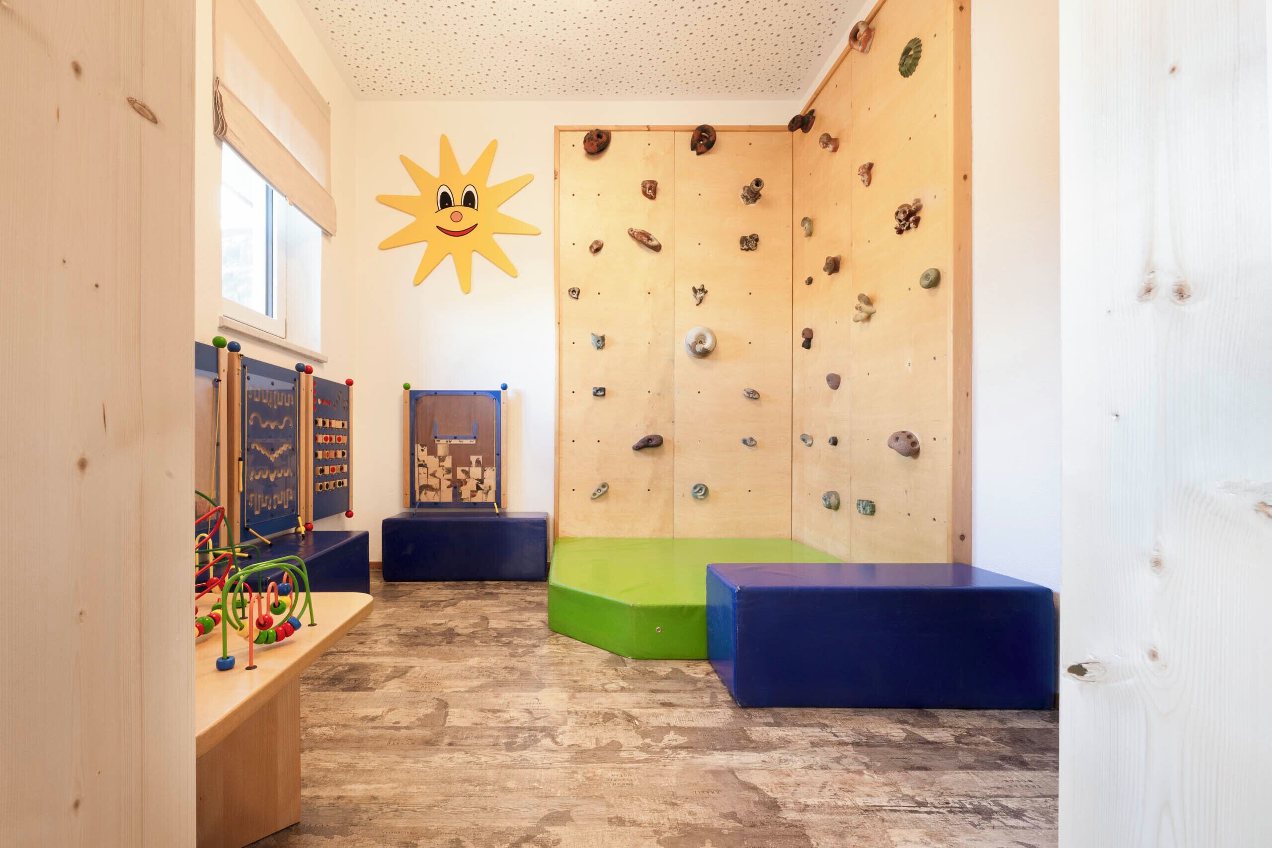 A climbing wall with various holds, a sun decoration, and a wooden floor.