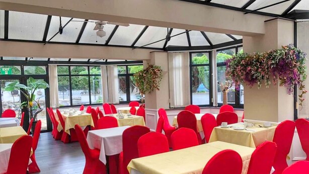 A restaurant with red chairs and tables, large windows, and hanging plants. - The Kensington Hotel (Bournemouth)