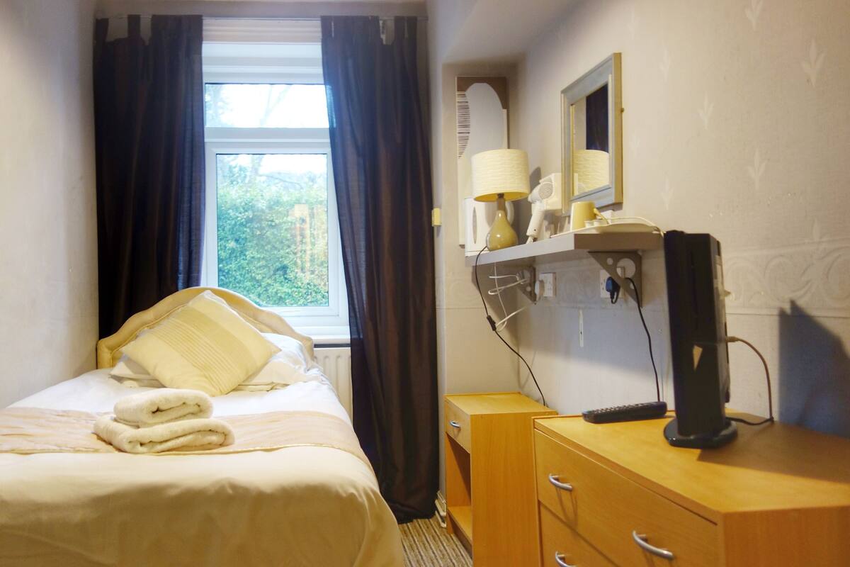 A hotel room with a bed, a wooden dresser, a mirror, and a window with curtains.