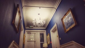 A hallway with a chandelier, framed pictures, and a door with a sign. - The Kensington Hotel (Bournemouth)