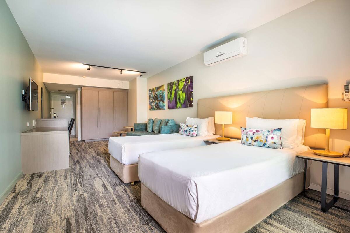 Habitación de hotel con dos camas, un escritorio, una silla, un espejo y obras de arte en la pared.