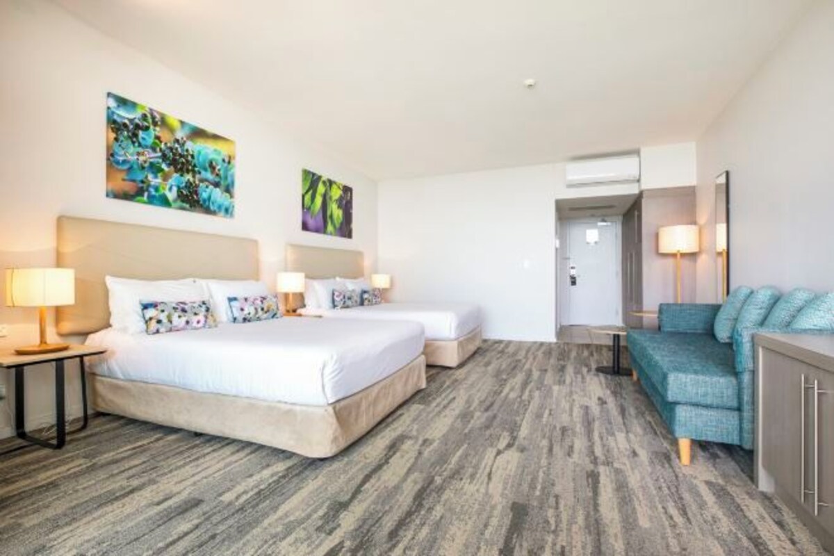Una habitación de hotel con dos camas, un sofá, un escritorio y obras de arte en las paredes.