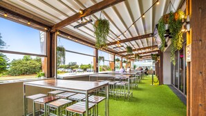 Un restaurante con terraza al aire libre, césped artificial verde, plantas colgantes y vistas a la calle.