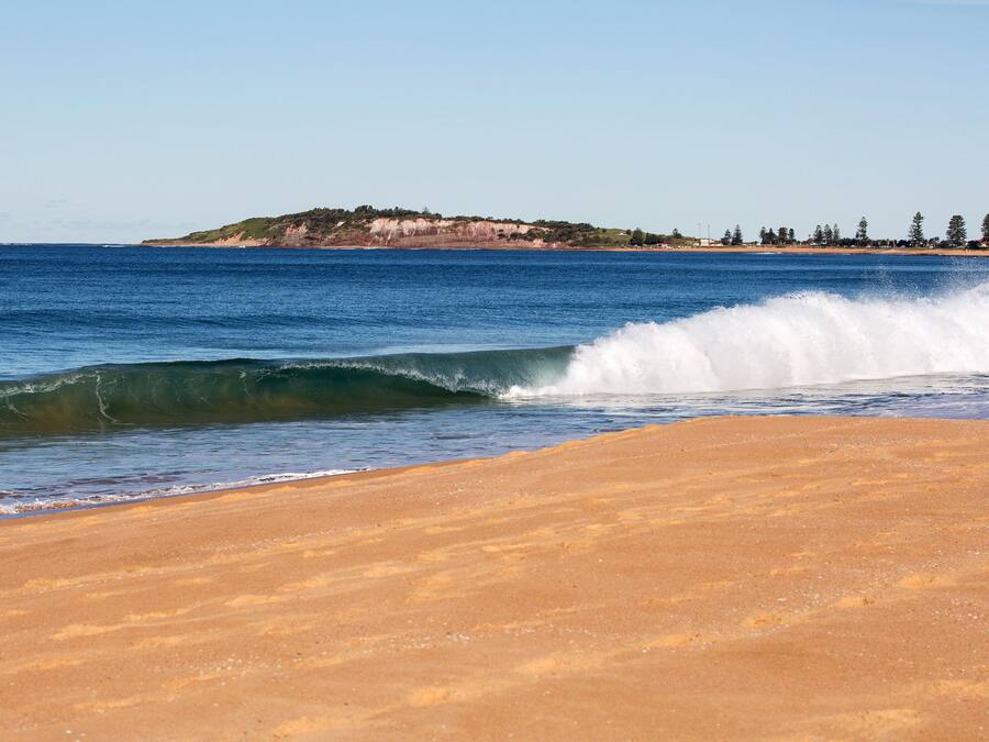 A beach with waves, a sandy shore, and a distant landmass with trees.