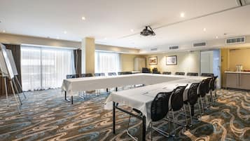 A conference room with a long table, chairs, a projector, and a large window with curtains.