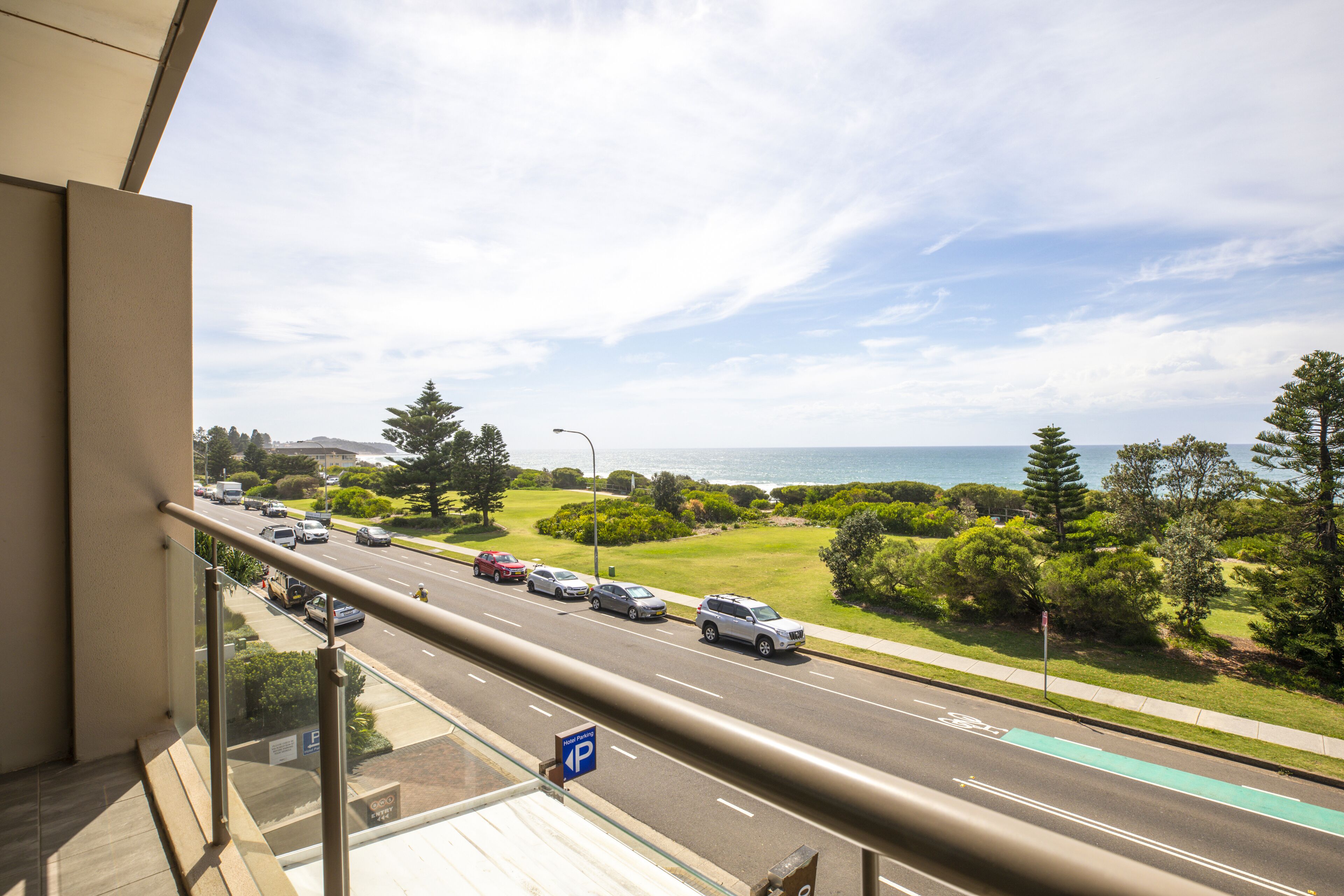Une vue depuis un balcon donnant sur une route où circulent des voitures, un panneau indiquant un parking et de la verdure.