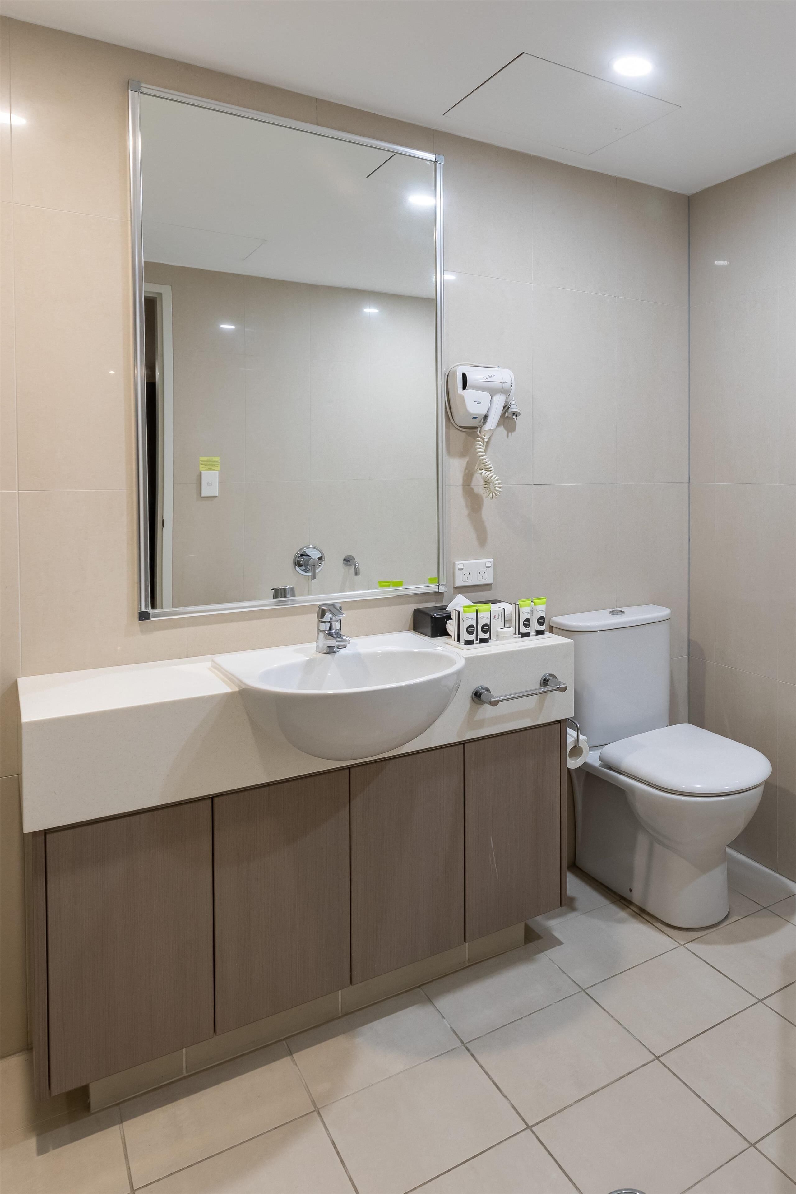 Een moderne badkamer met een witte wastafel, spiegel en toilet.
