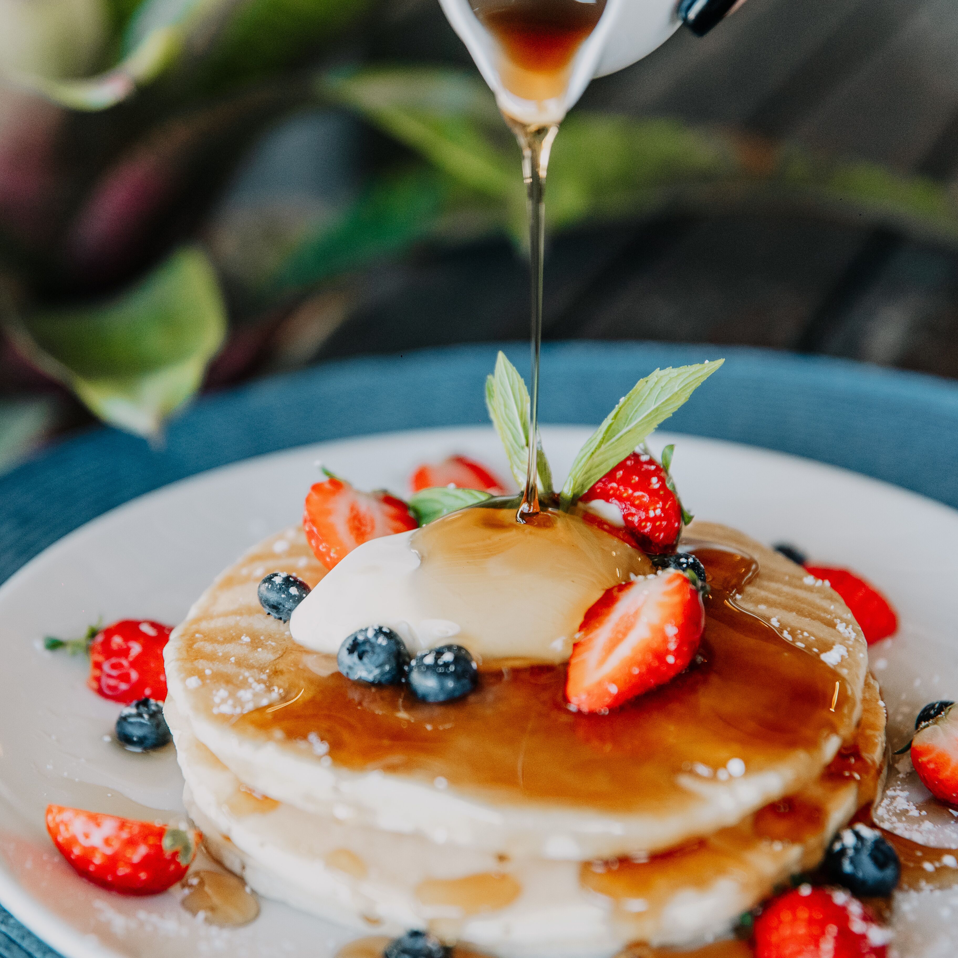 A stack of pancakes with a dollop of cream and fresh berries on top, drizzled with syrup.