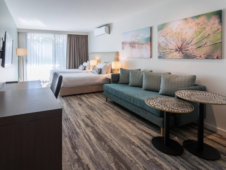 A hotel room with a bed, a sofa, two side tables, a desk, and a large window with curtains.