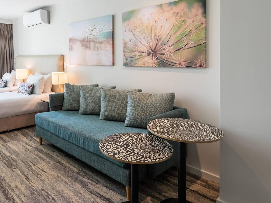 A hotel room with a bed, a sofa, two side tables, and two wall-mounted lamps.