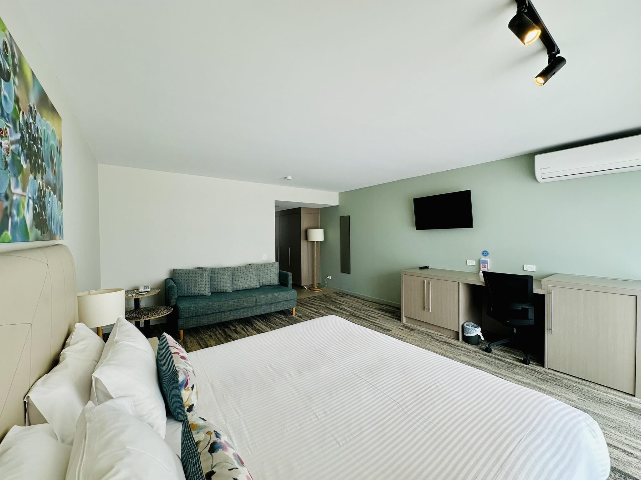 A hotel room with a large bed, a desk, a television, and a painting on the wall.