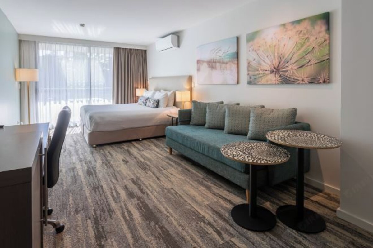 Una habitación de hotel con una cama, un sofá, dos mesitas, un escritorio y una silla.