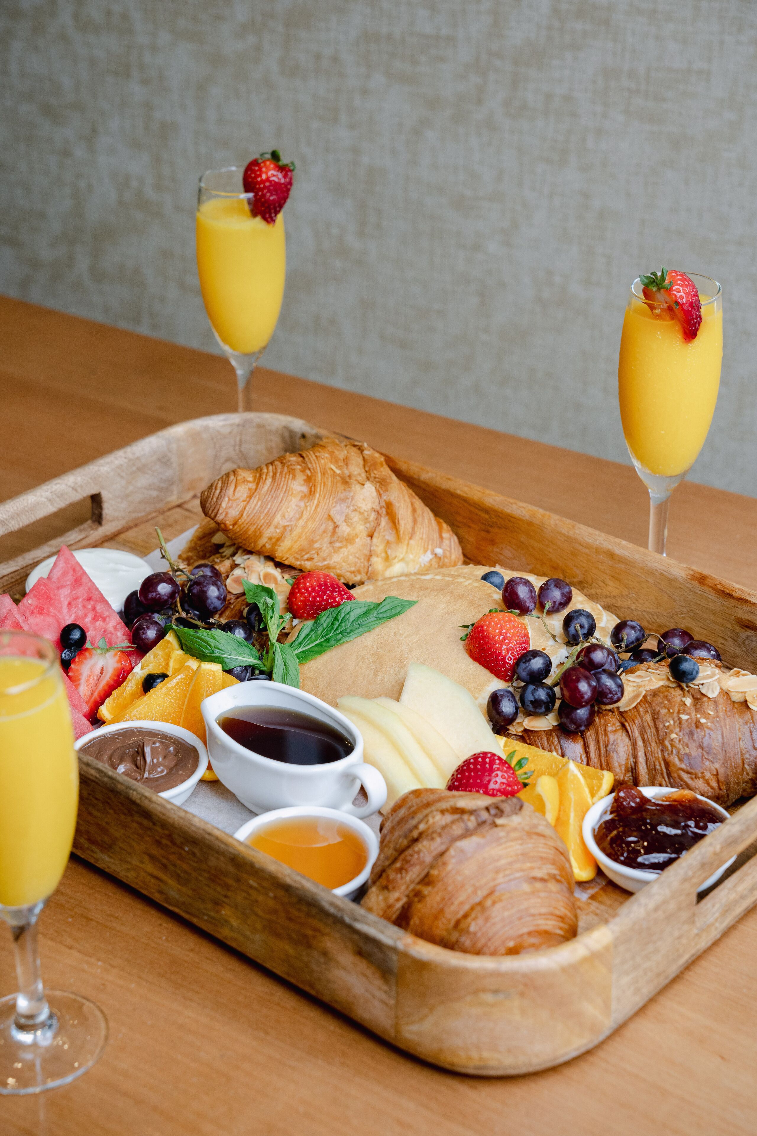 Ein Frühstücksbrett mit Croissants, Früchten und Getränken.