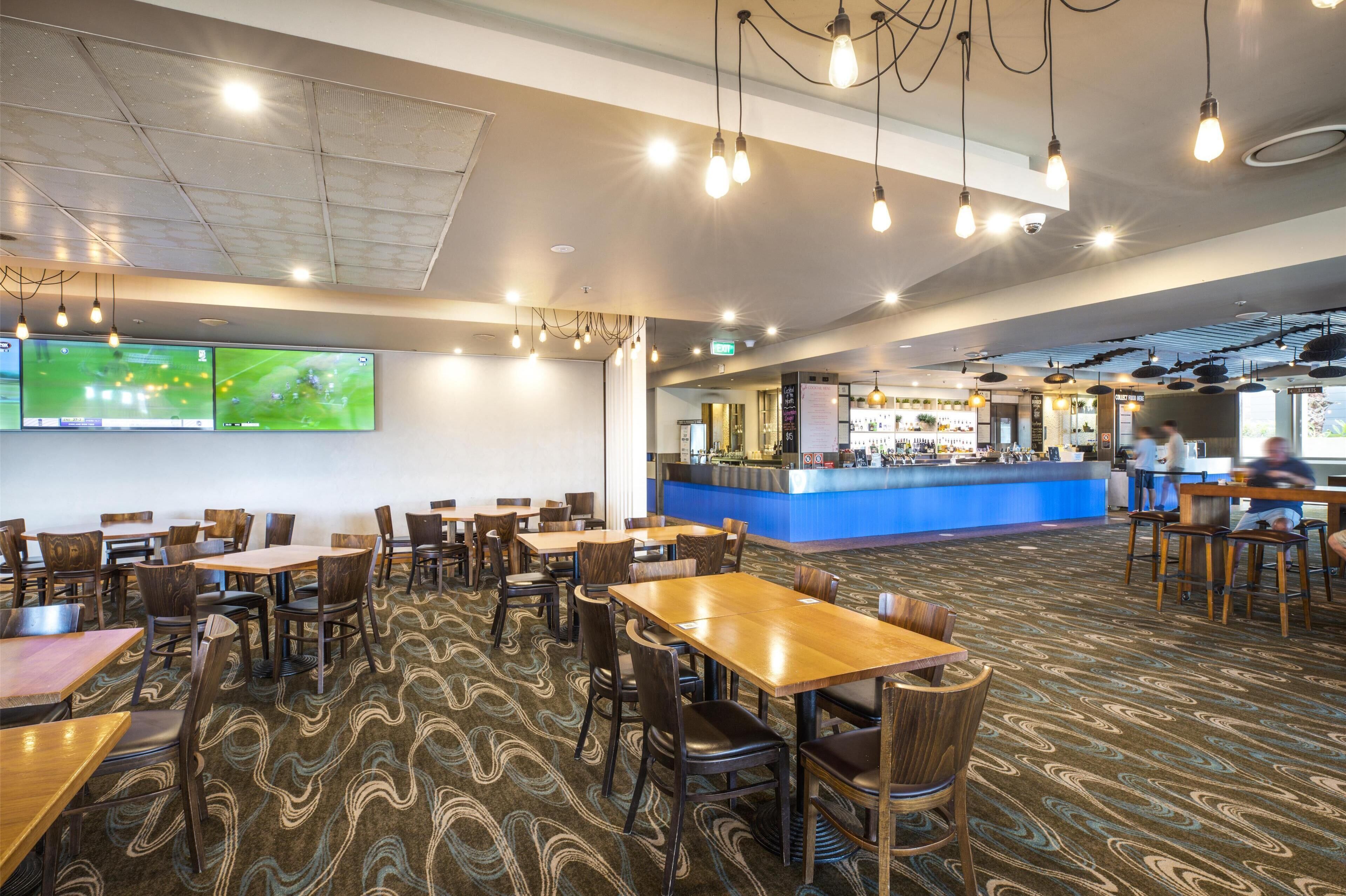 A spacious restaurant with multiple tables and chairs, a counter area with a blue countertop, and a patterned carpet.