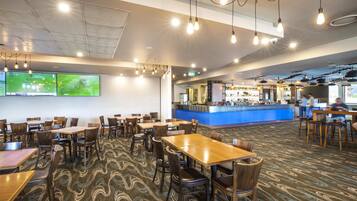 A spacious restaurant with multiple tables and chairs, a counter area with a blue countertop, and a patterned carpet.