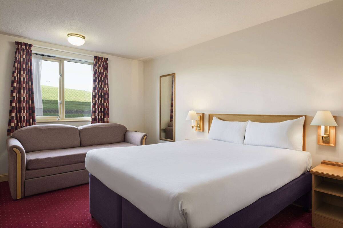Une chambre d’hôtel avec un grand lit, un canapé, une table de chevet et une fenêtre avec des rideaux.