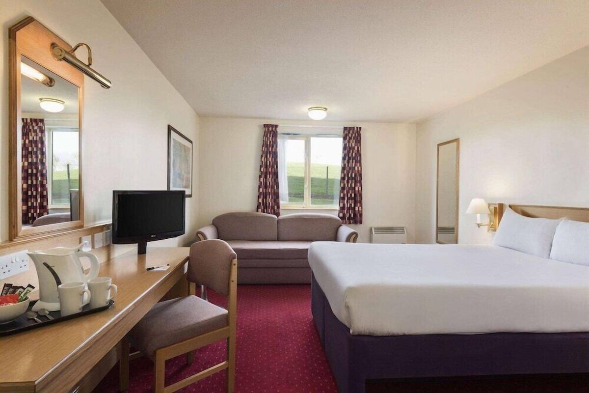 Une chambre d’hôtel comprenant un lit, un bureau avec un ordinateur, une chaise, une fenêtre avec des rideaux et un miroir.