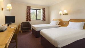 Habitación de hotel con dos camas, un escritorio con televisor, una silla y una ventana con cortinas.