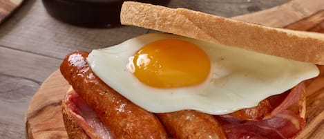 A breakfast plate with a fried egg, sausages, and bacon on a wooden board.