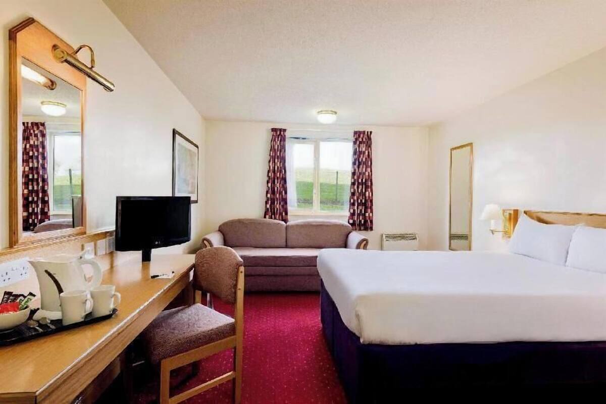 Une chambre d’hôtel avec un lit, un bureau avec un ordinateur, une chaise, une télévision et une fenêtre avec des rideaux.