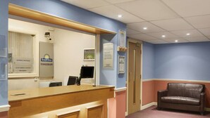 Zona de recepción con escritorio, una silla y un cartel de Days Inn Tewkesbury.