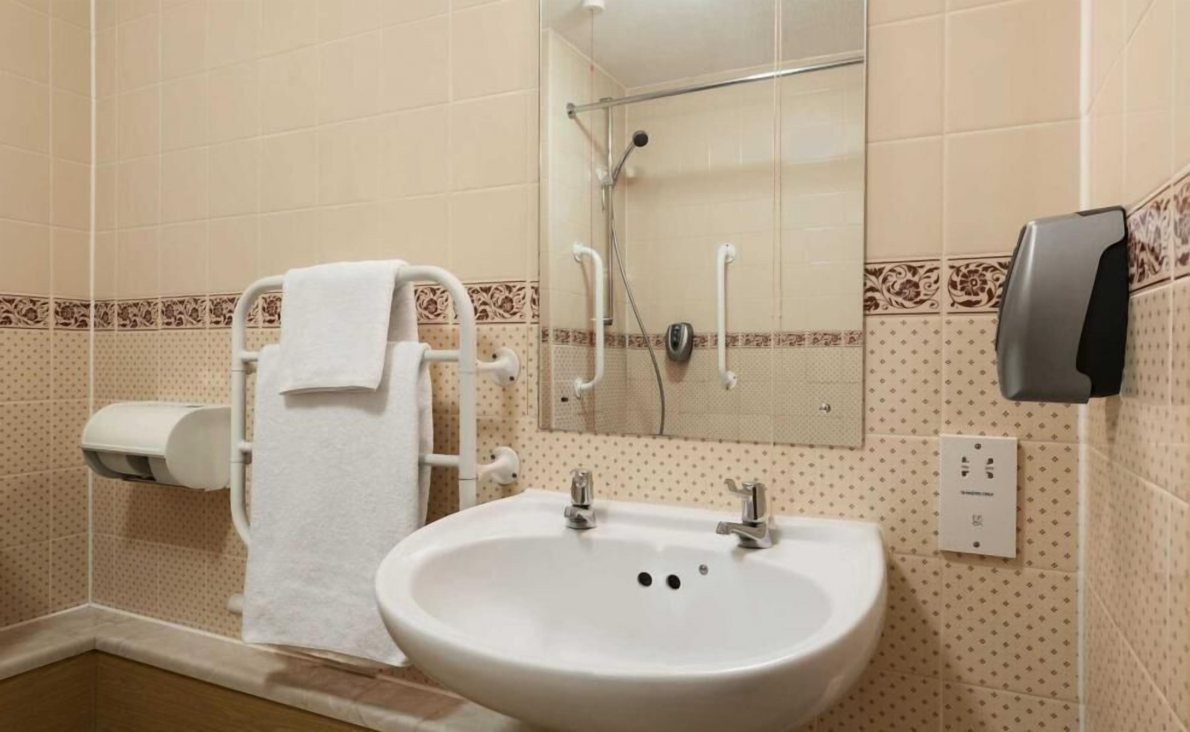 A bathroom with a sink, a towel rack, a shower, and a soap dispenser.