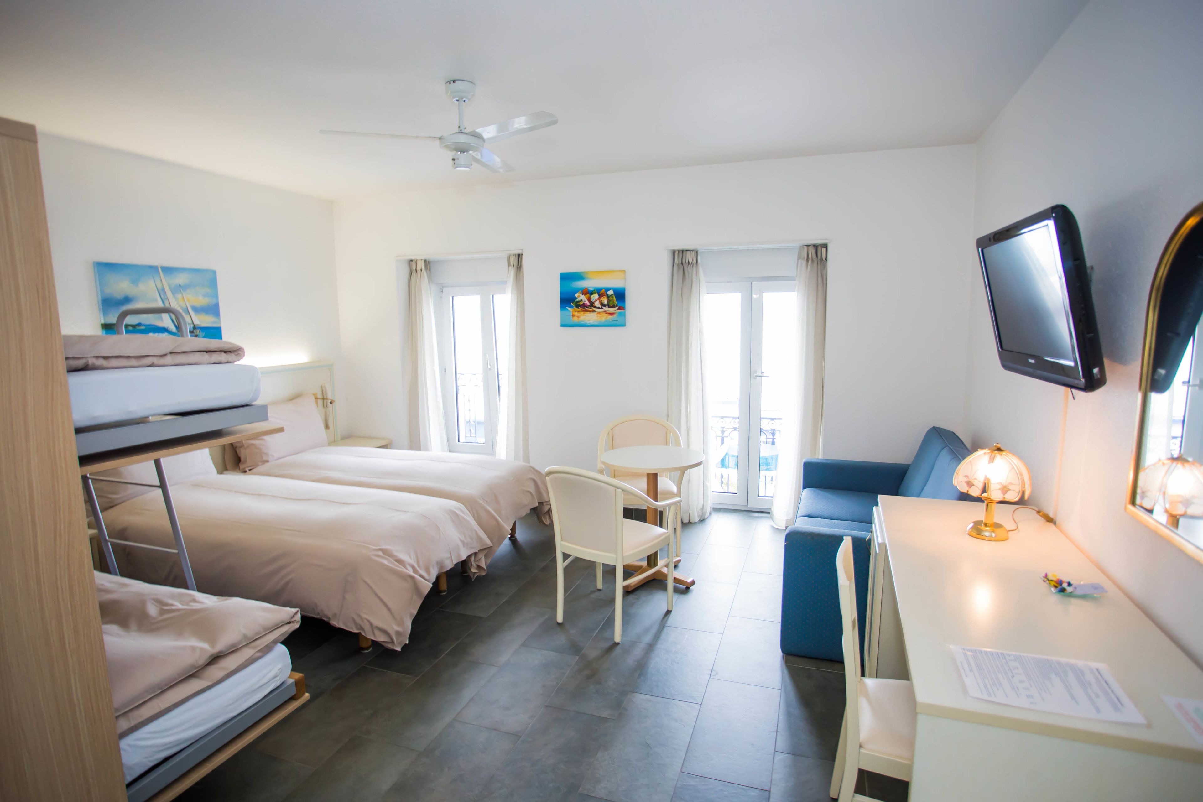 Een hotelkamer met stapelbedden, een bureau, een stoel, een televisie en een plafondventilator.