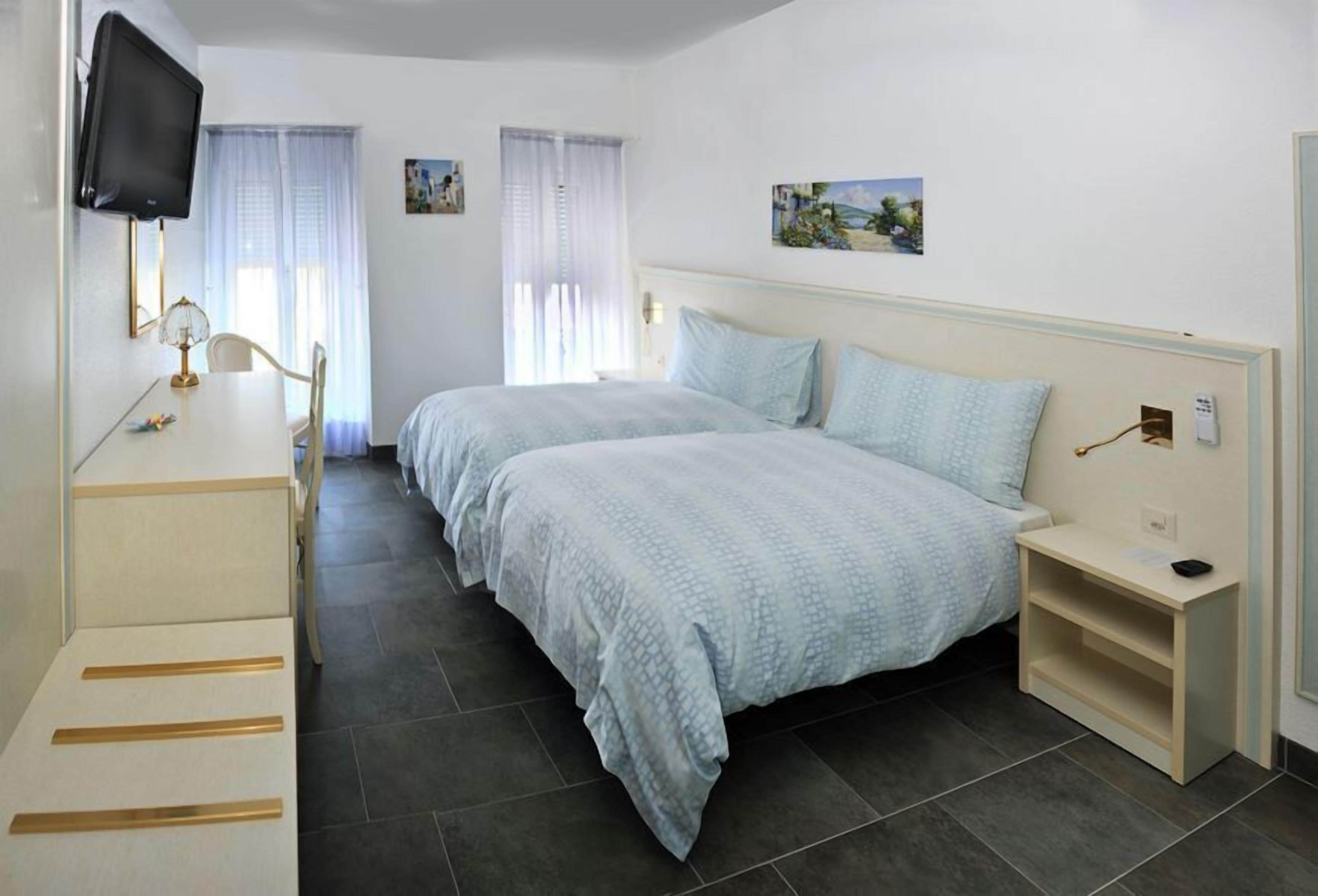 Habitación de hotel con dos camas, un escritorio con silla, un televisor montado en la pared y una mesita de noche.