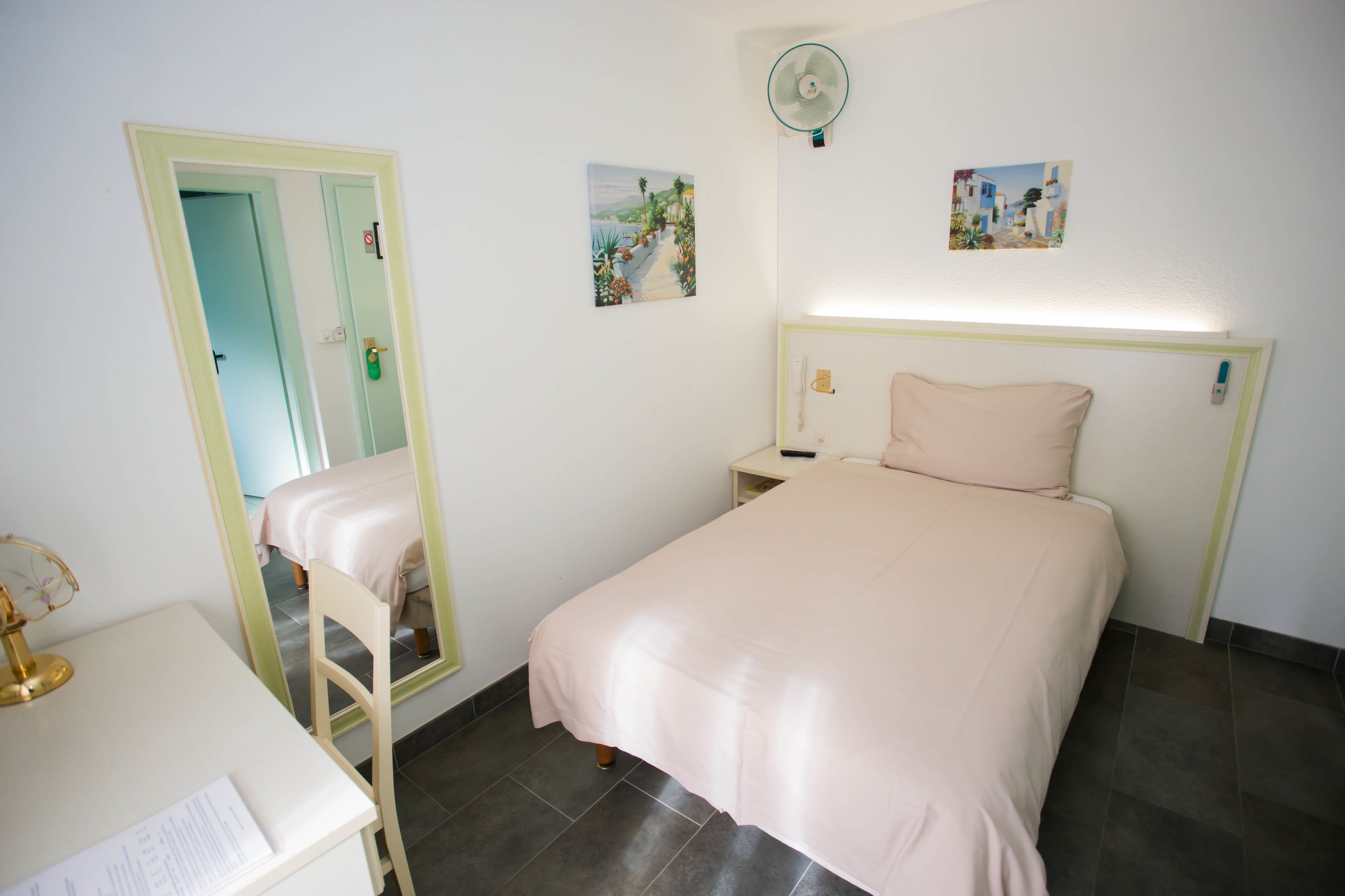 Un dormitorio con cama, escritorio, silla, espejo y dos cuadros en la pared.