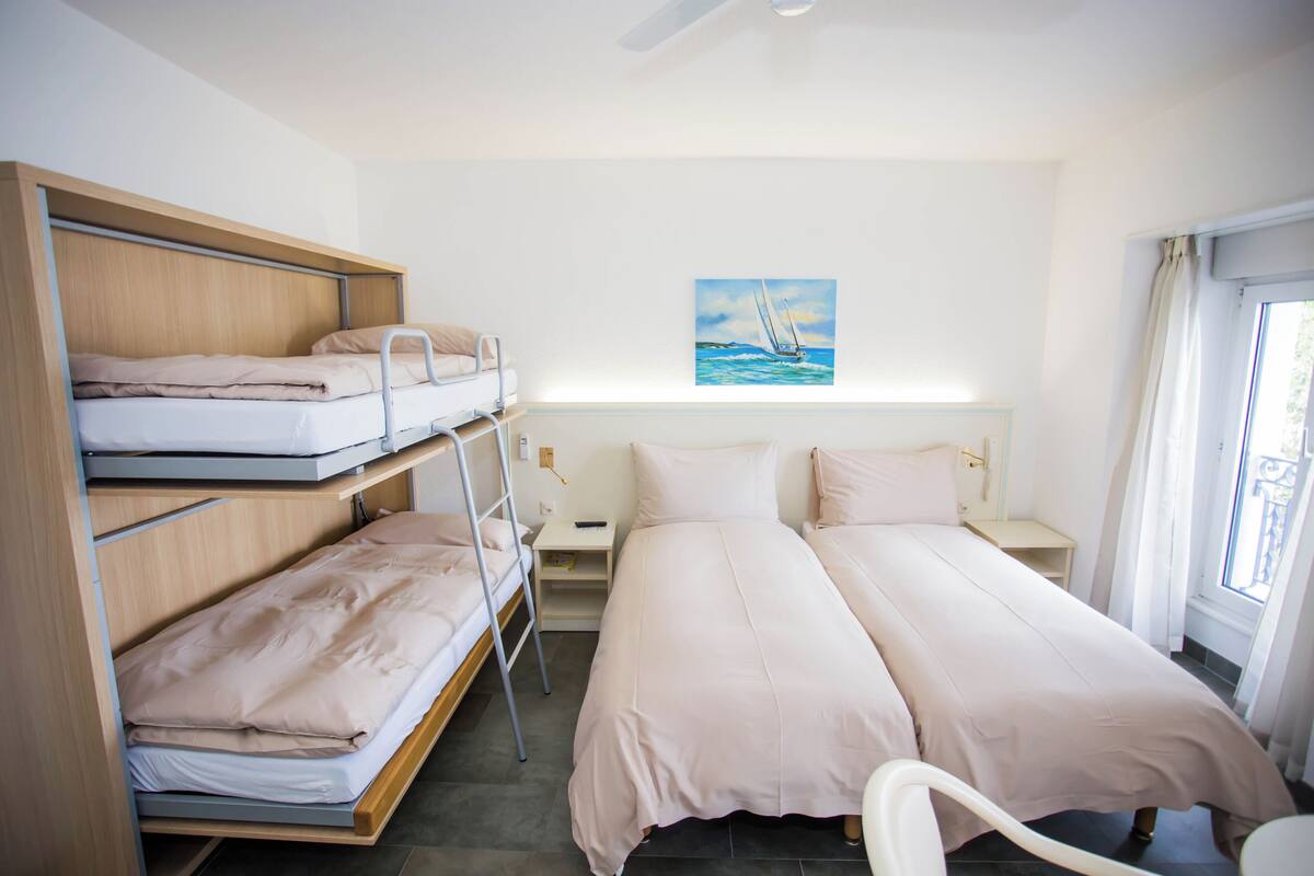 A room with bunk beds, a bedside table, a chair, and a painting of a sailboat on the wall.