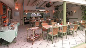 A restaurant with green chairs and tables, a small cart with magazines, and a view of the outside through large windows. - Hotel Du Port (Villeneuve)