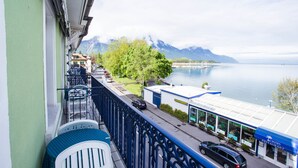 A balcony with a view of a lake, a restaurant, and mountains in the background. - Hotel Du Port (Villeneuve)