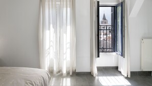 A bedroom with a bed, a window with a view of a church, and sheer curtains. - Hotel Du Port (Villeneuve)
