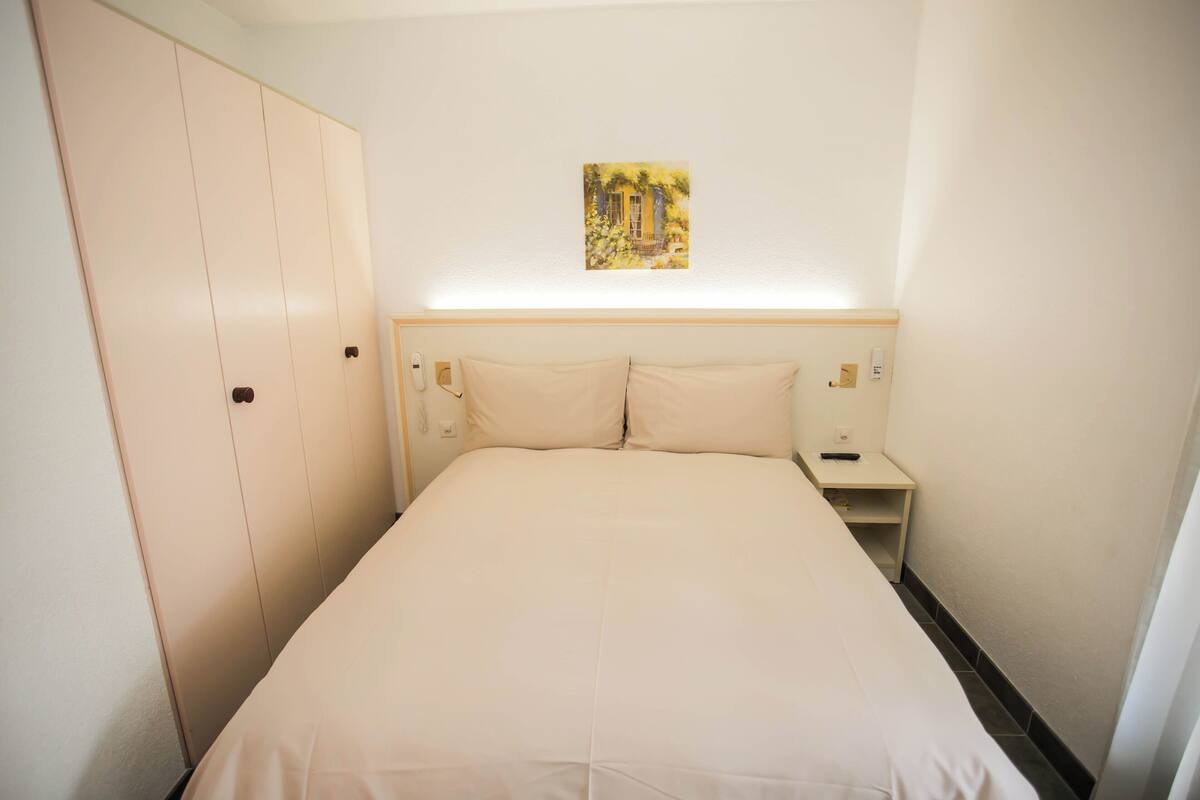 A hotel room with a bed, a nightstand, a wardrobe, and a painting on the wall.