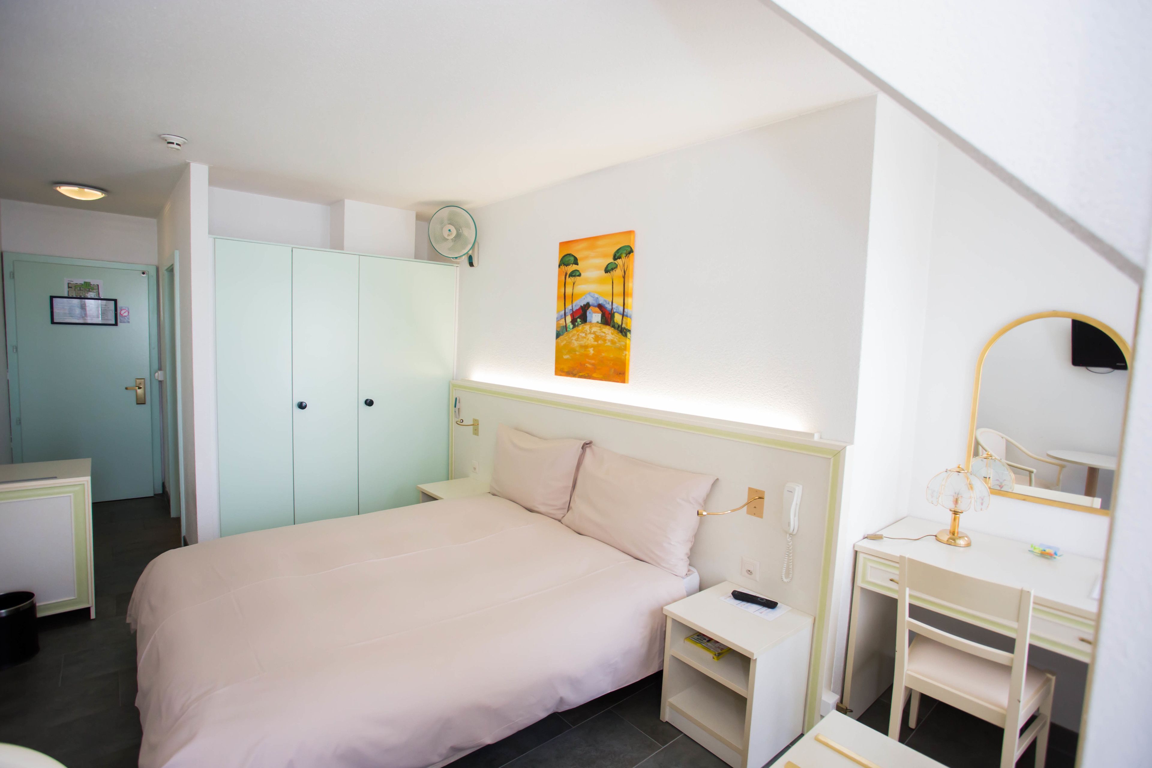 A bedroom with a bed, bedside tables, a desk with a chair, a wardrobe, and a painting on the wall.