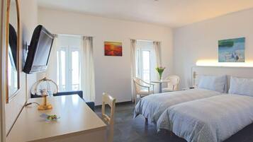 A hotel room with two beds, a desk with a computer, a chair, and a small table with a vase of flowers.