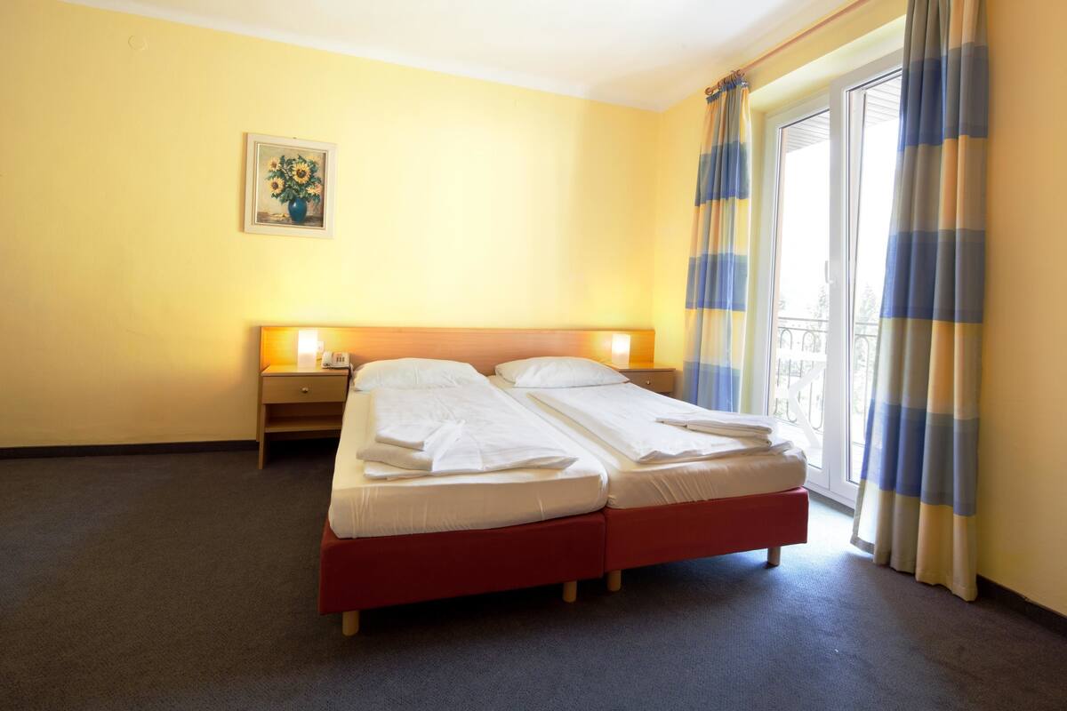 Un lit double avec une base rouge, une table de chevet avec une lampe et une fenêtre avec des rideaux.