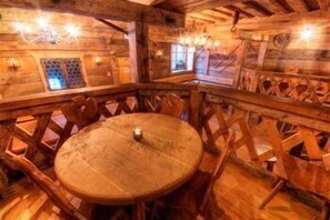 Un intérieur en bois avec une table ronde et des chaises, des poutres en bois au plafond et une fenêtre offrant une vue.