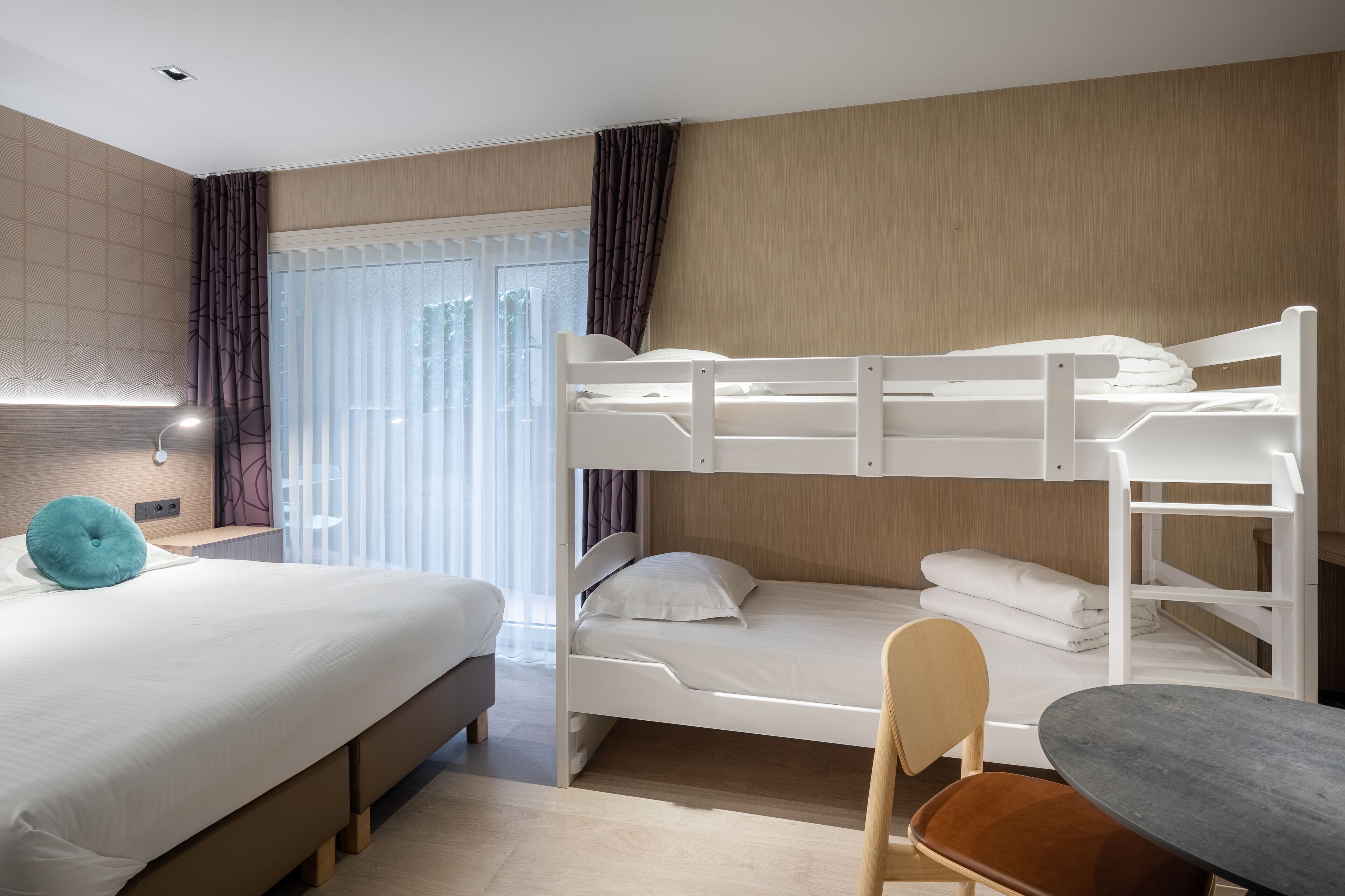 Une chambre d’hôtel avec un lit superposé, un lit simple, un bureau et une chaise.
