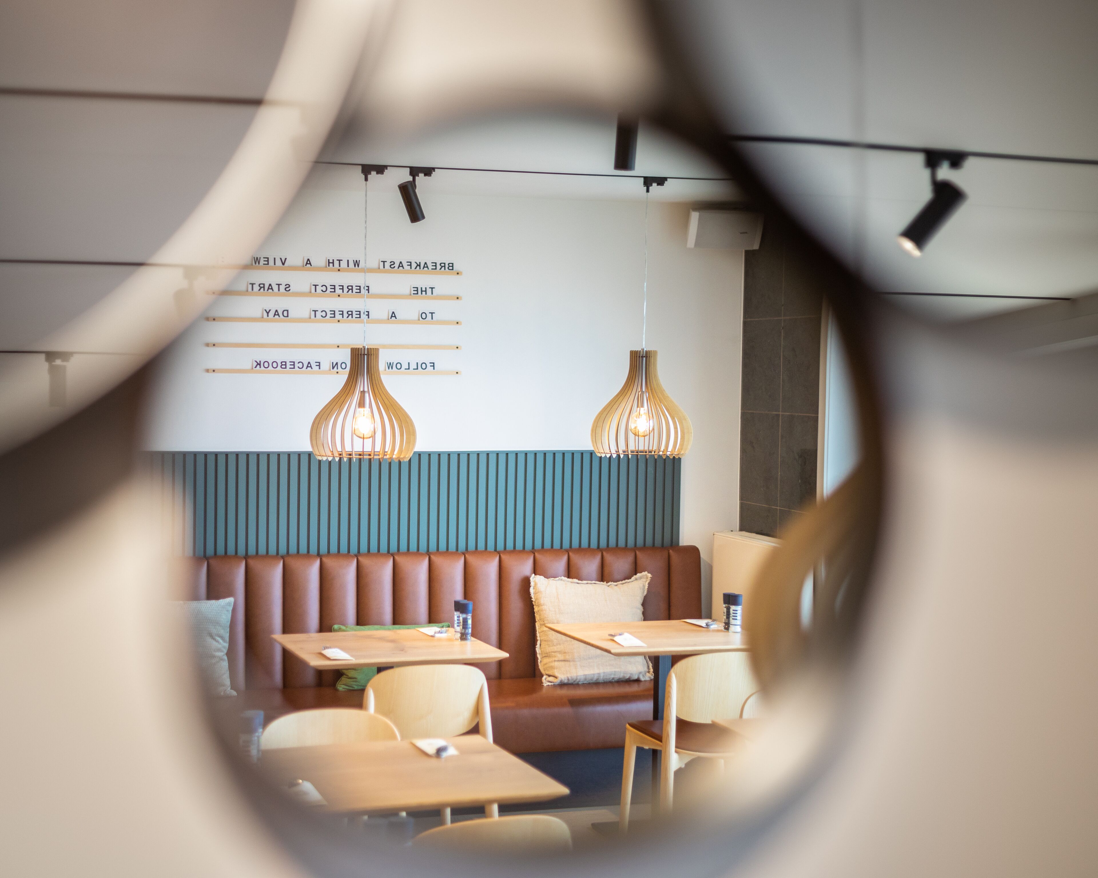 L’intérieur d’un restaurant présente un coin salon avec des bancs en bois, des luminaires suspendus et un tableau affichant le menu sur le mur.