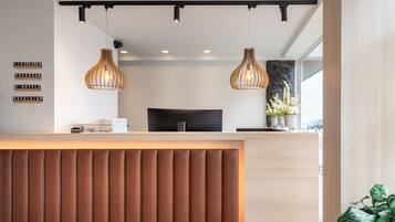 A modern reception desk with a wooden panel design, two pendant lights, a flat-screen TV, and a wall-mounted sign with social media handles.