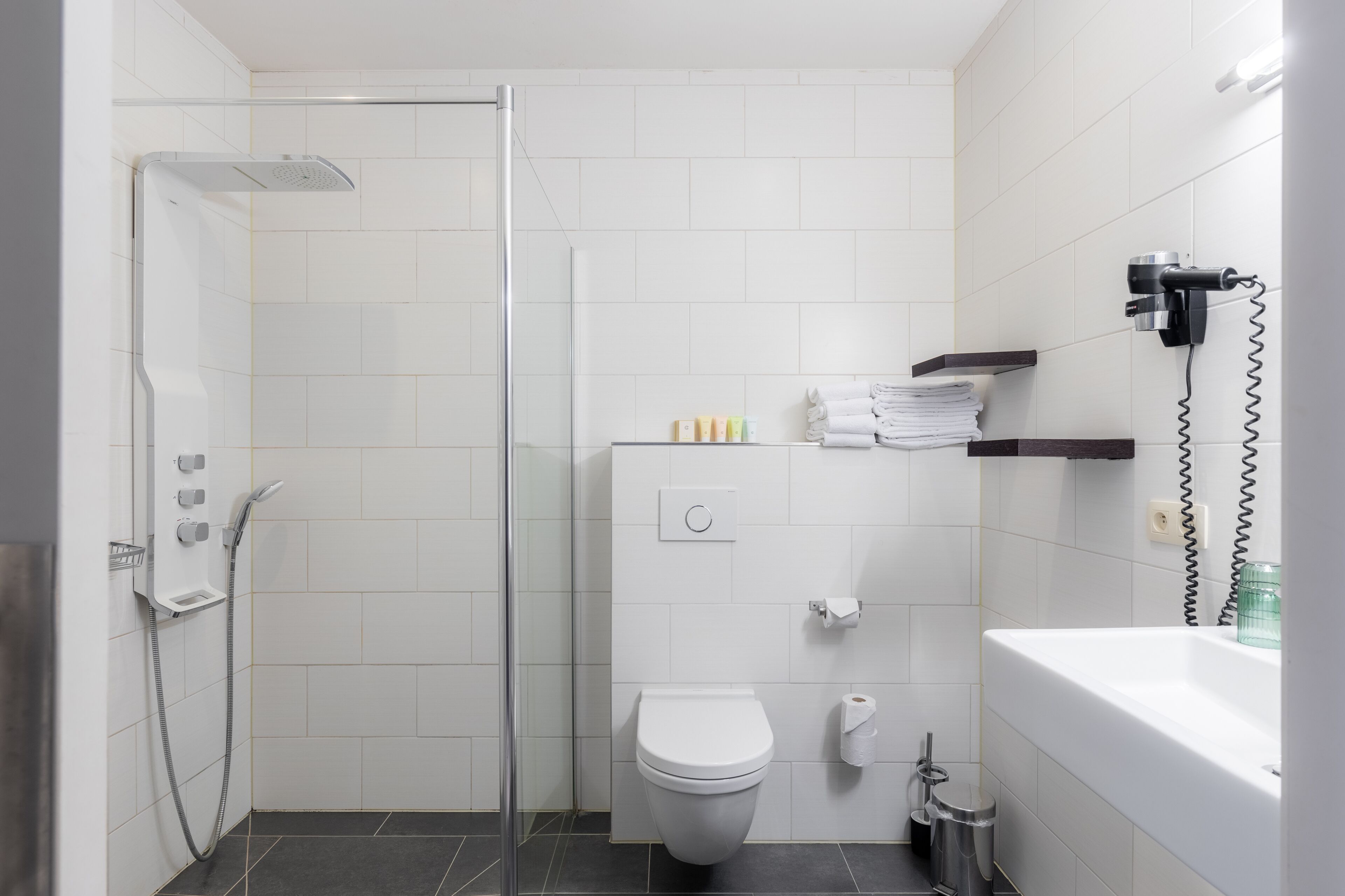 Un baño moderno con ducha de vidrio, inodoro blanco y lavamanos con toallero.