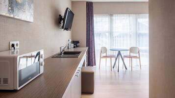 Una cocina moderna con microondas, lavamanos y un televisor de pantalla plana montado en la pared. Hay una zona de comedor con una mesa redonda y dos sillas.