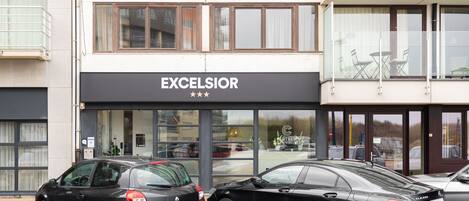 A building with a sign reading "EXCELSIOR" and two parked cars in front.